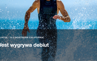 Triathlonista w stroju startowym wybiega z wody, woda rozpryskuje sie wokol