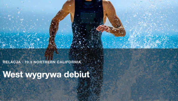 Triathlonista w stroju startowym wybiega z wody, woda rozpryskuje sie wokol